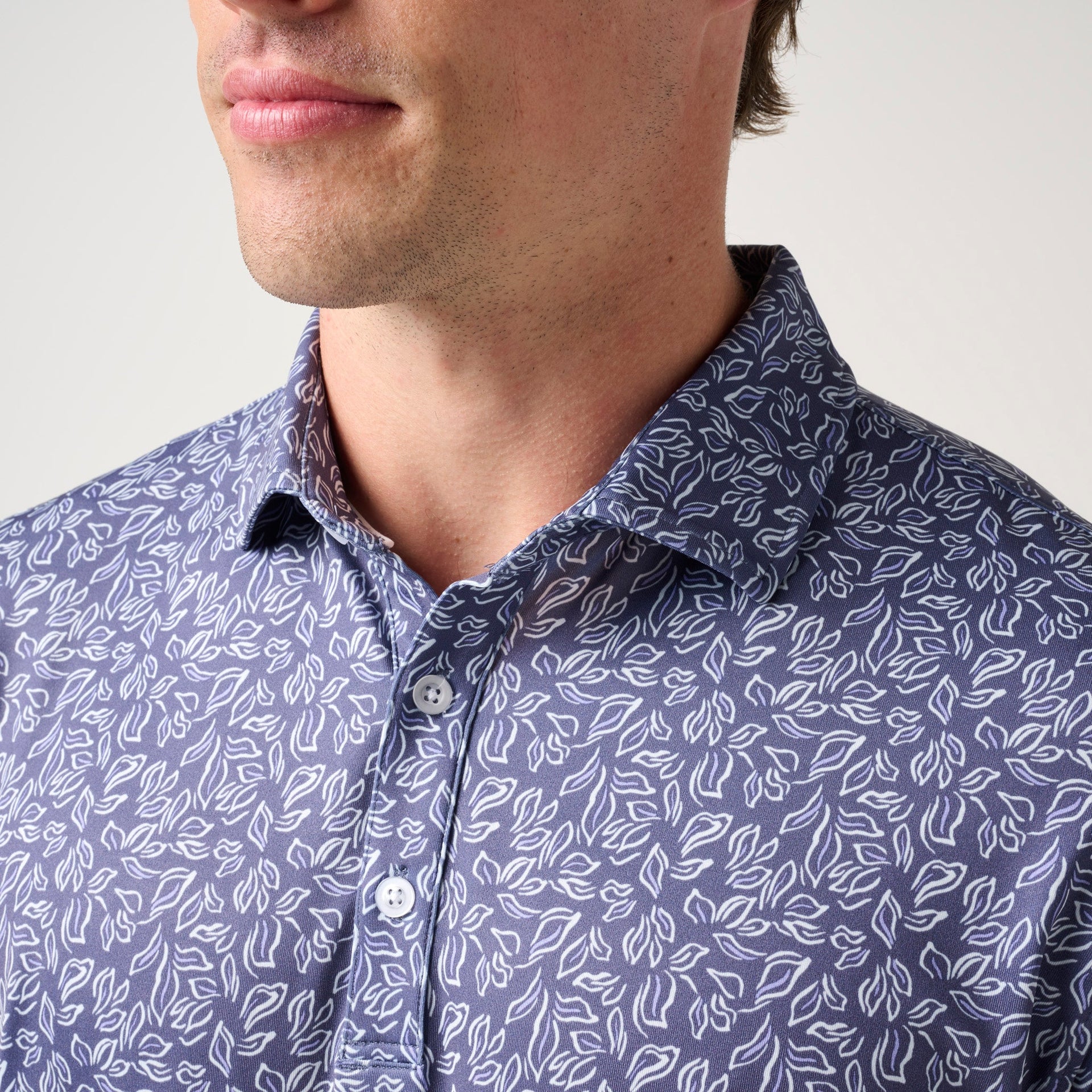 Navy polo shirt with white floral leaf pattern and button front closure.