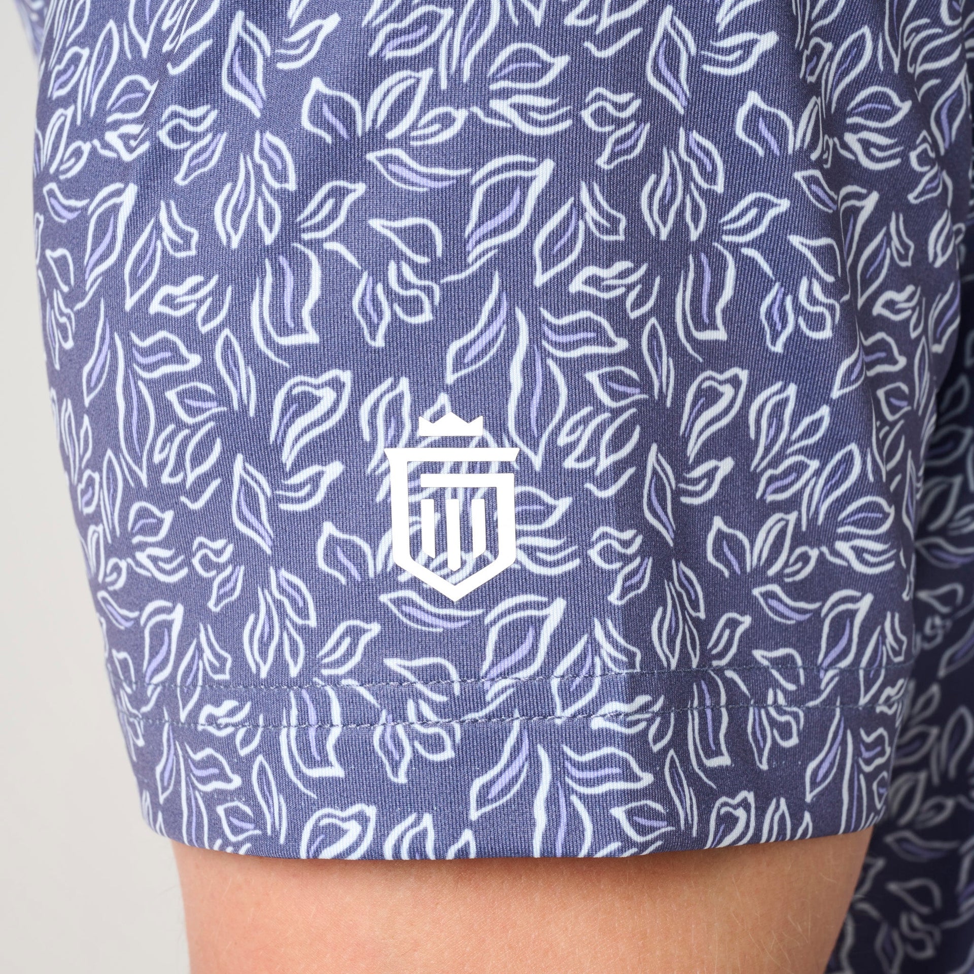 Navy polo shirt with white leaf pattern and embroidered crest on chest.