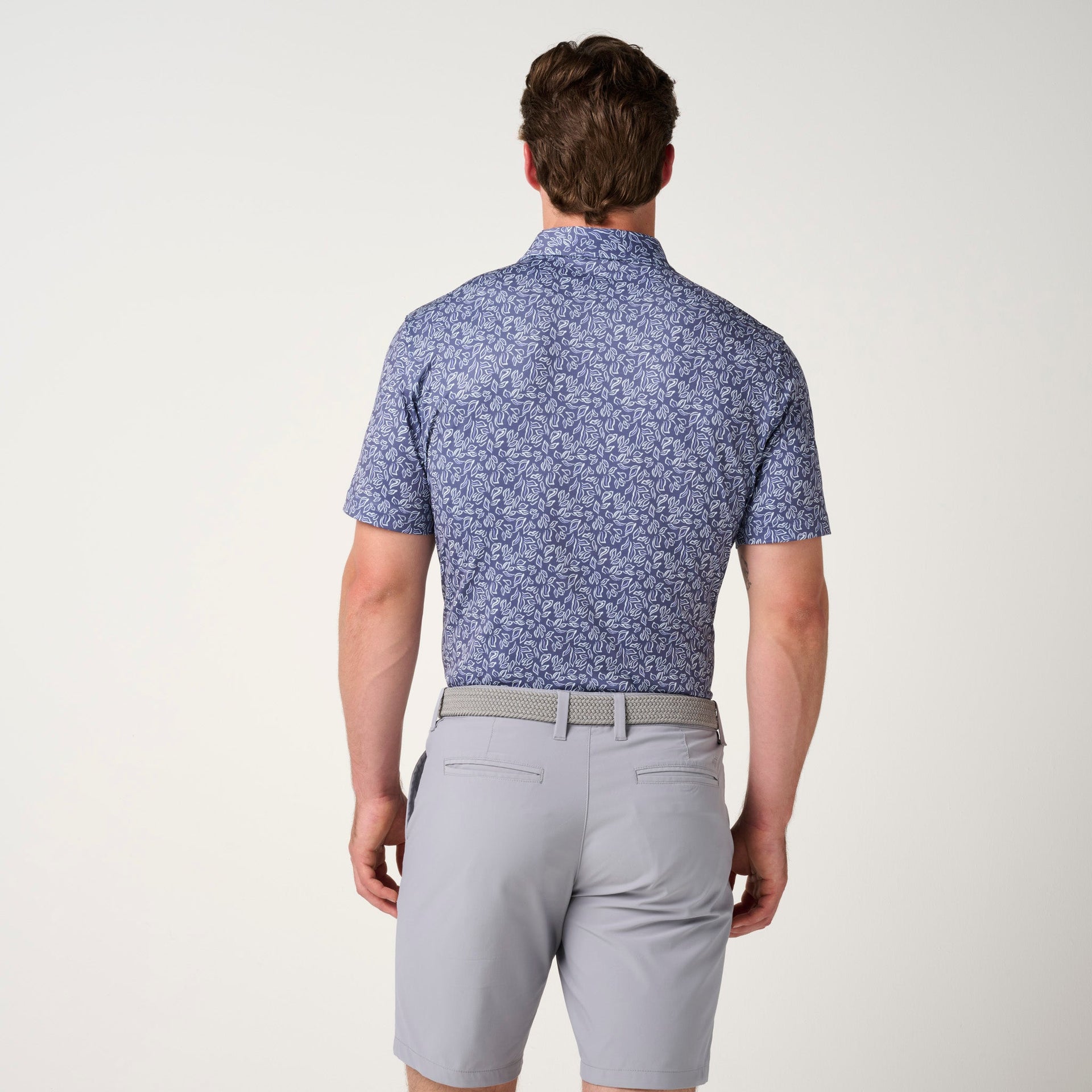 Blue floral polo shirt with short sleeves worn with gray shorts and a beige belt.
