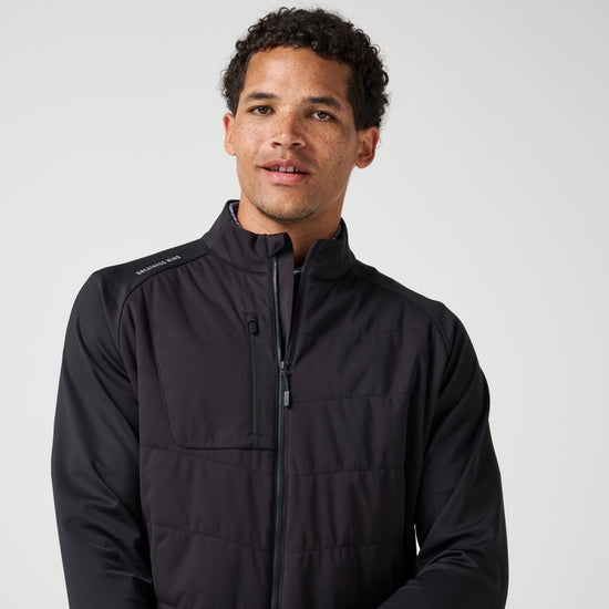 Man wearing black hybrid jacket with front zip closure and chest pocket against neutral background.