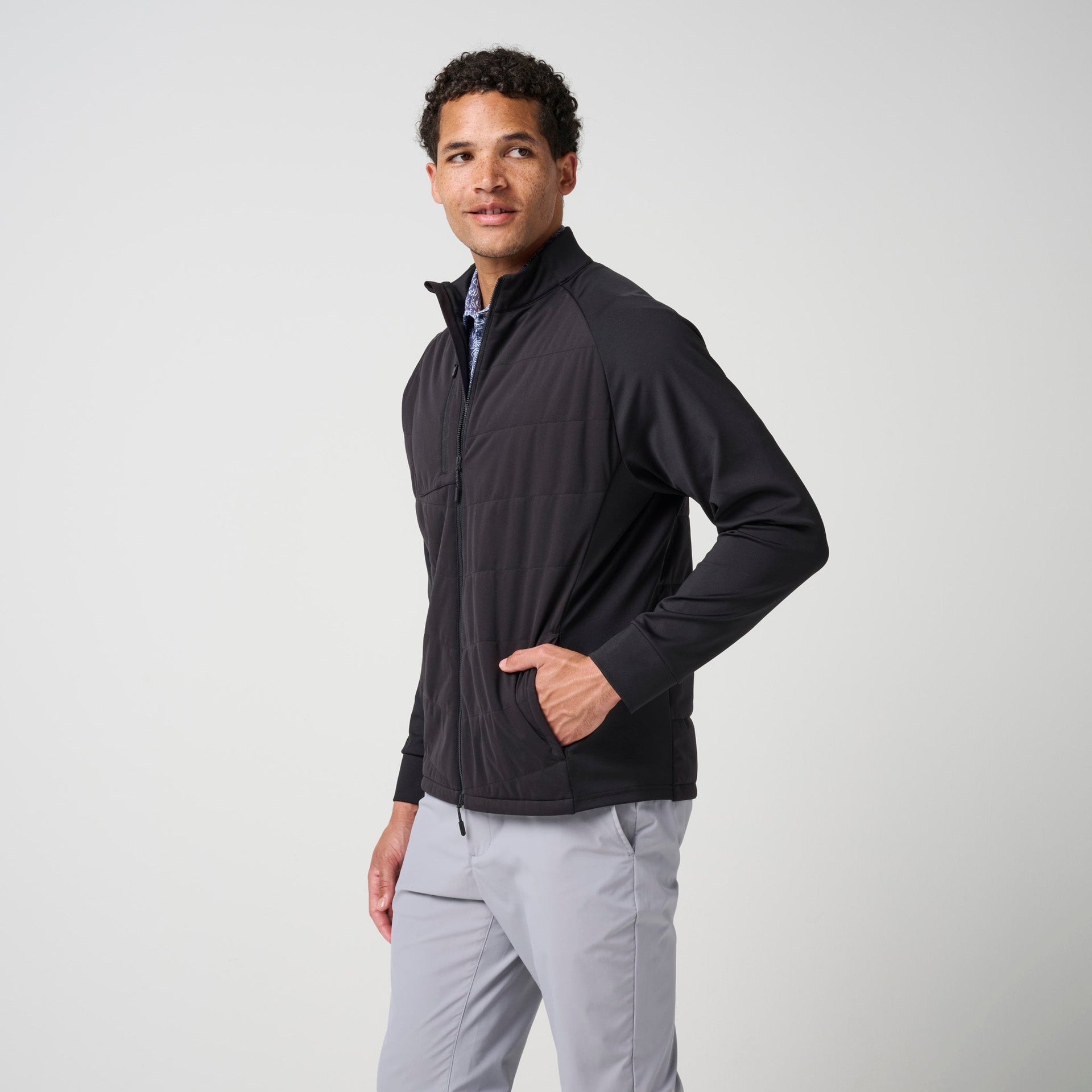 Black hybrid jacket with quilted torso and stretch knit sleeves, worn with light gray pants.