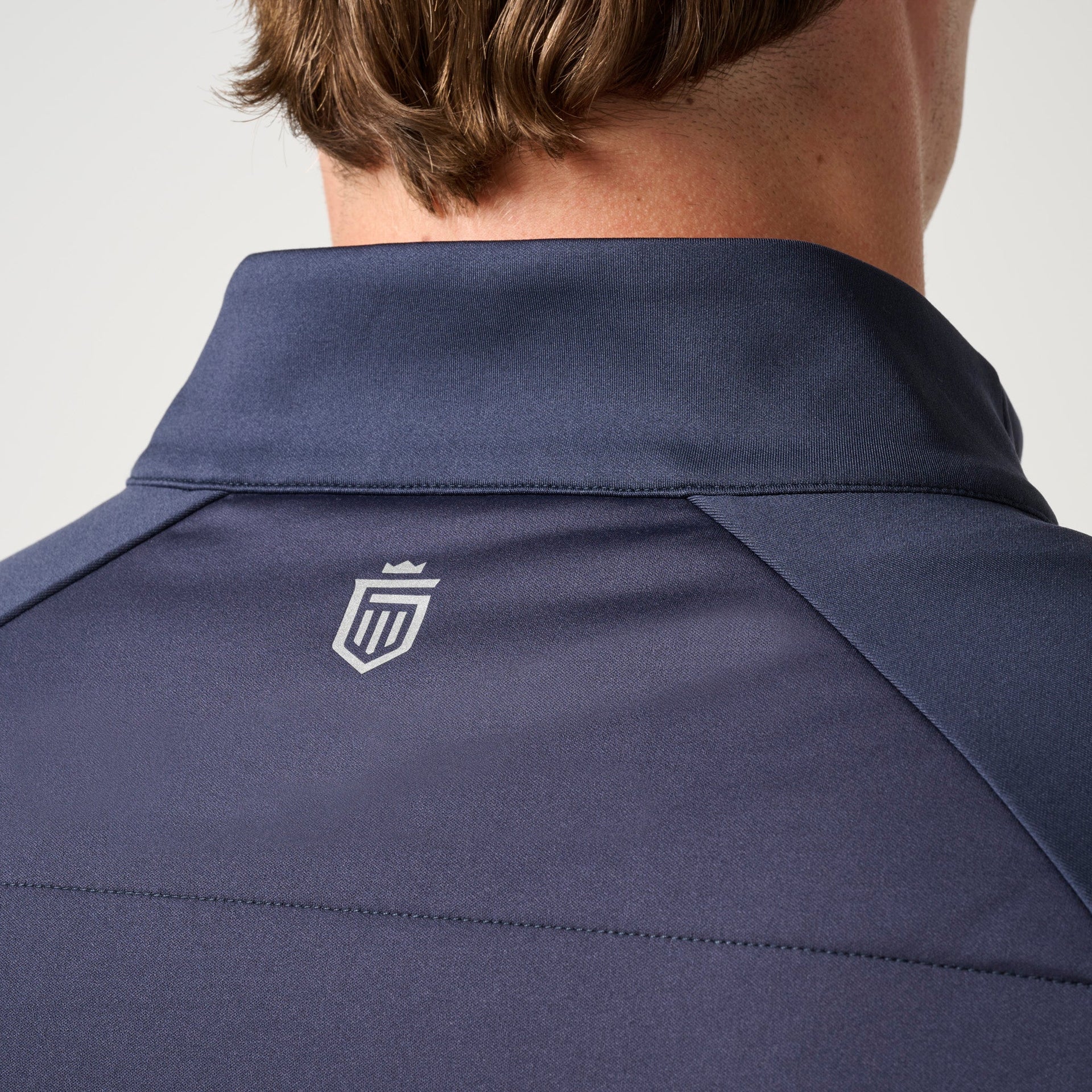 Navy blue hybrid jacket with shield logo on back, shown on person from shoulders up.
