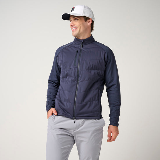 Navy quilted hybrid jacket with full-length zipper and knit sleeves on male model wearing light gray pants.