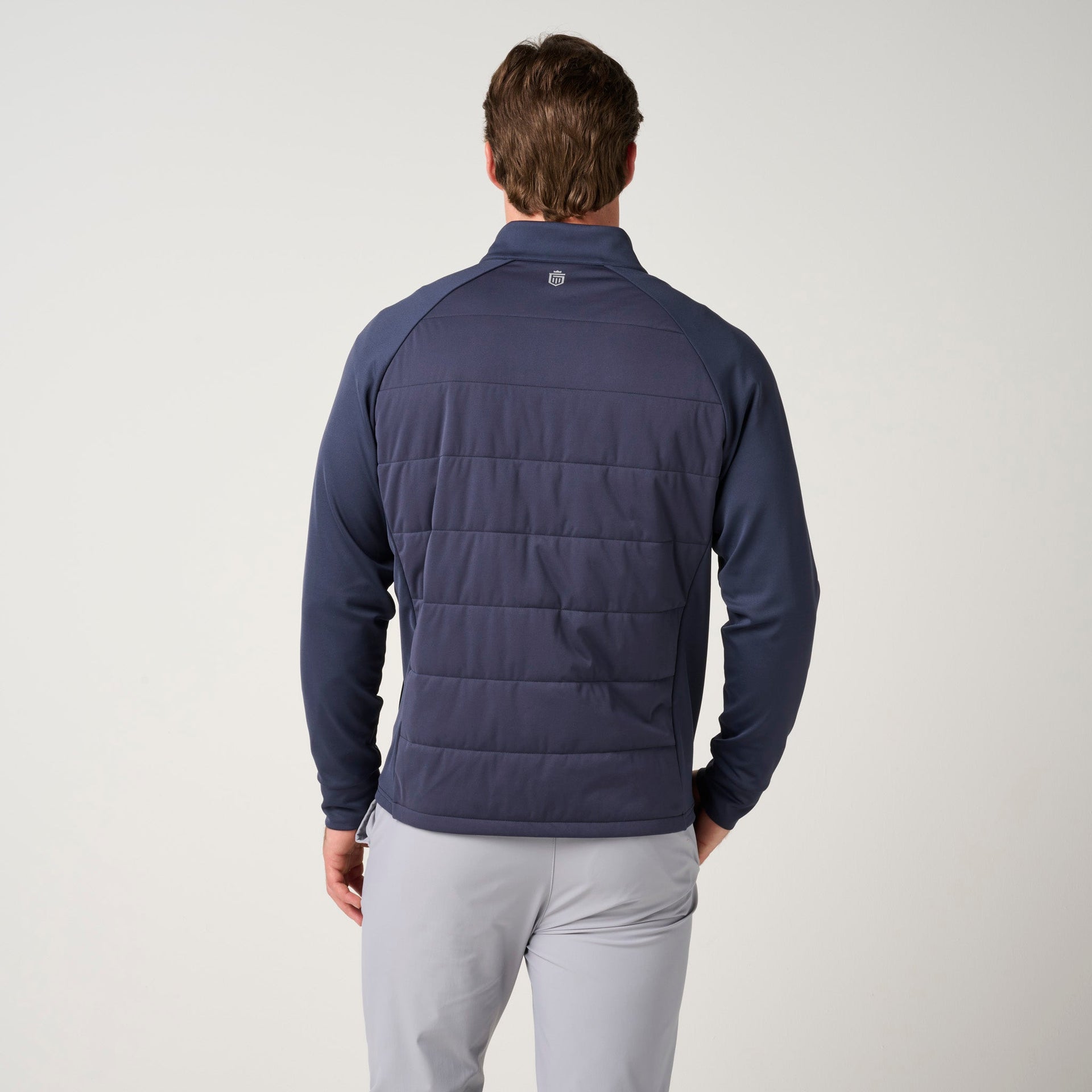 Navy hybrid jacket with quilted back panel and knit sleeves on male model wearing light gray pants.