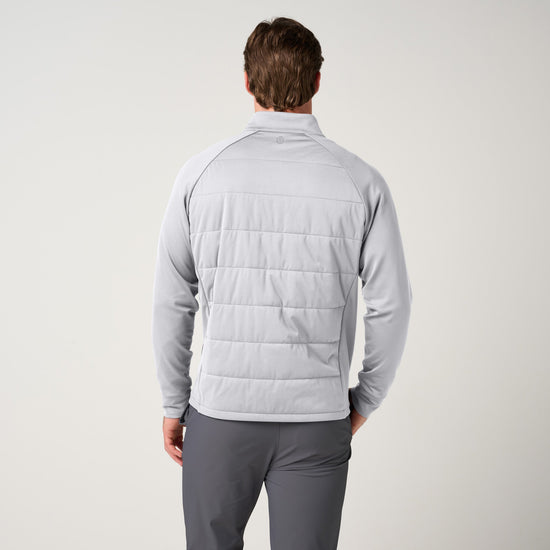 Man wearing light gray hybrid jacket with quilted back panel and knit sleeves, paired with charcoal pants, shown from behind.