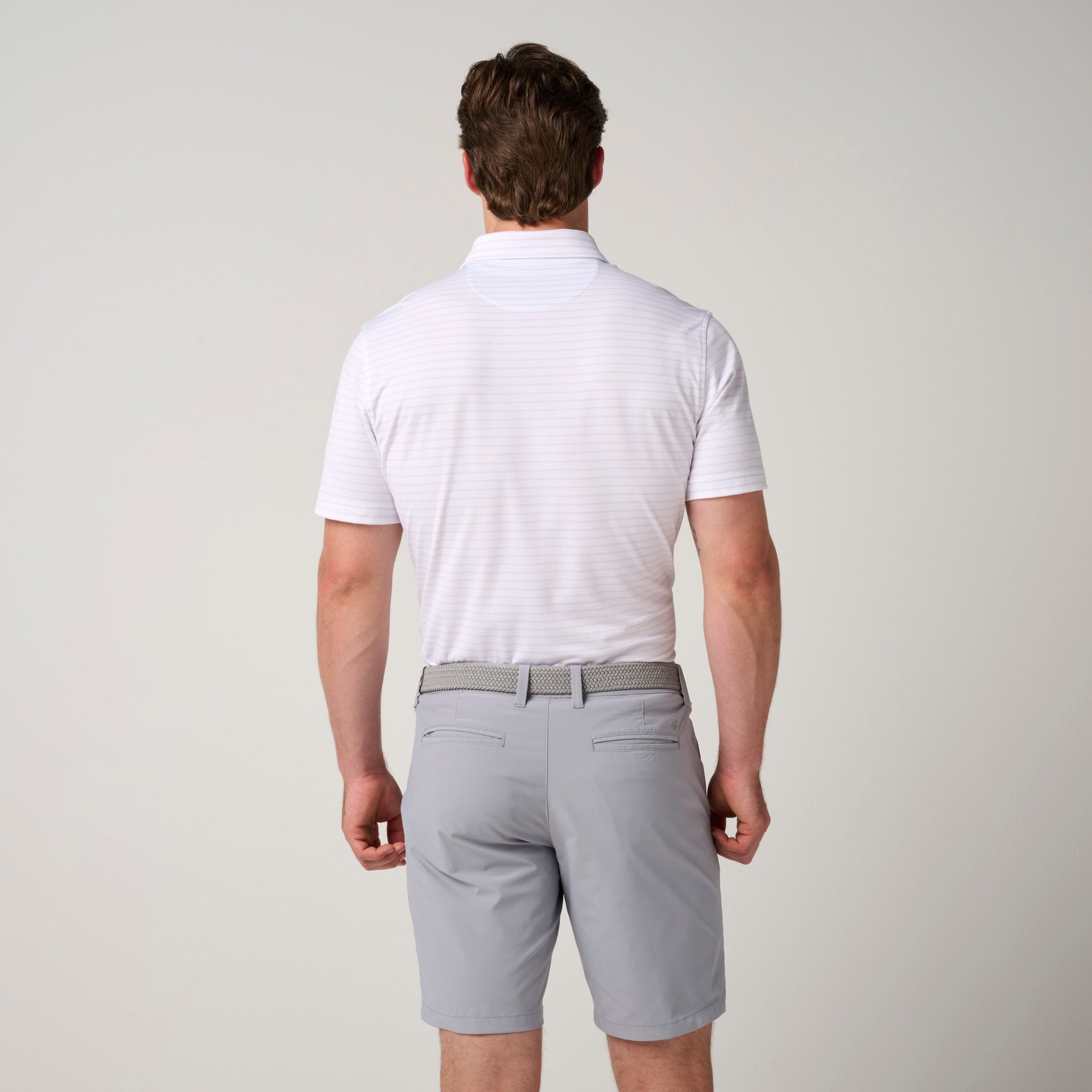 Man wearing white mesh polo shirt with horizontal stripes and gray shorts with belt, shown from back.