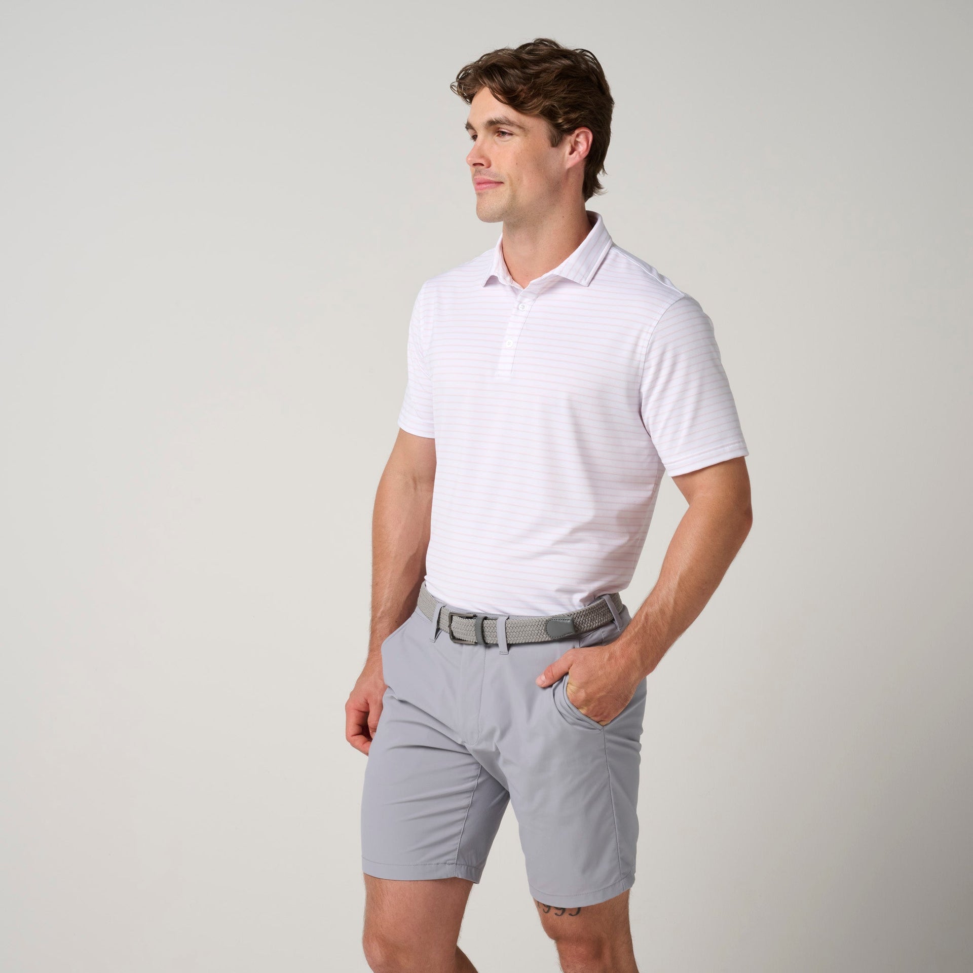 Man wearing white striped short-sleeve polo shirt with collar and gray shorts with belt.