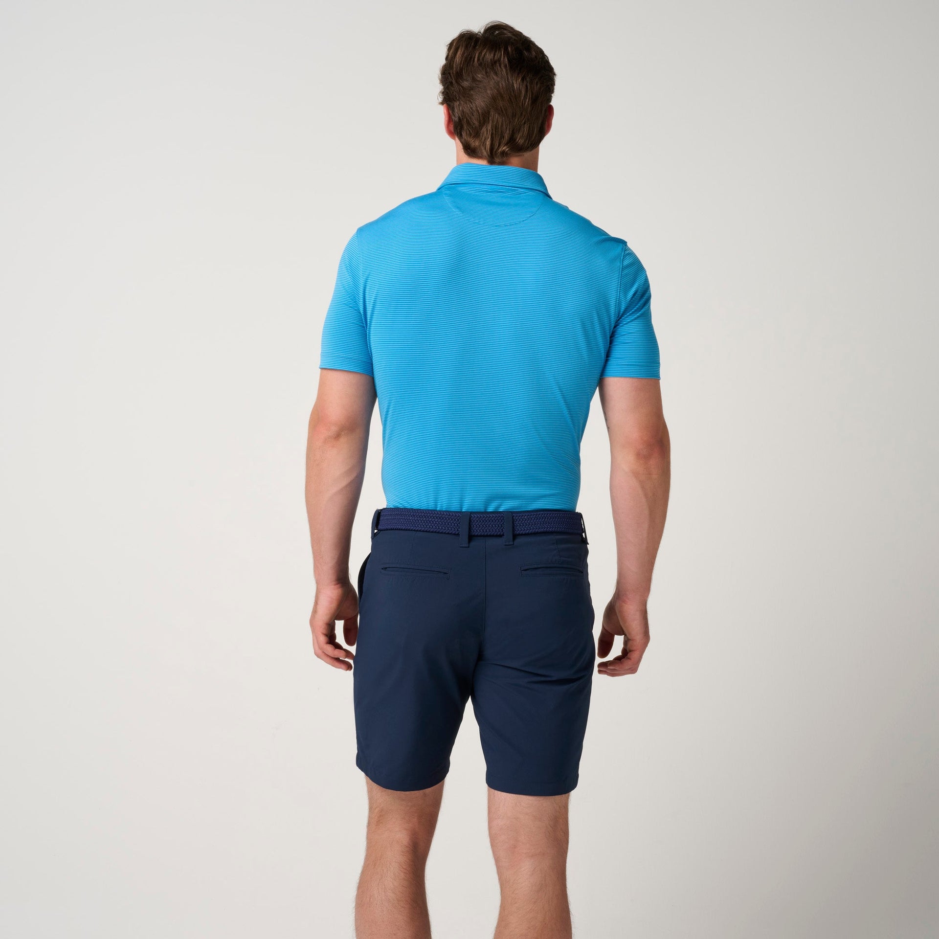 Man wearing bright blue short-sleeve polo shirt with textured fabric and navy shorts, back view.