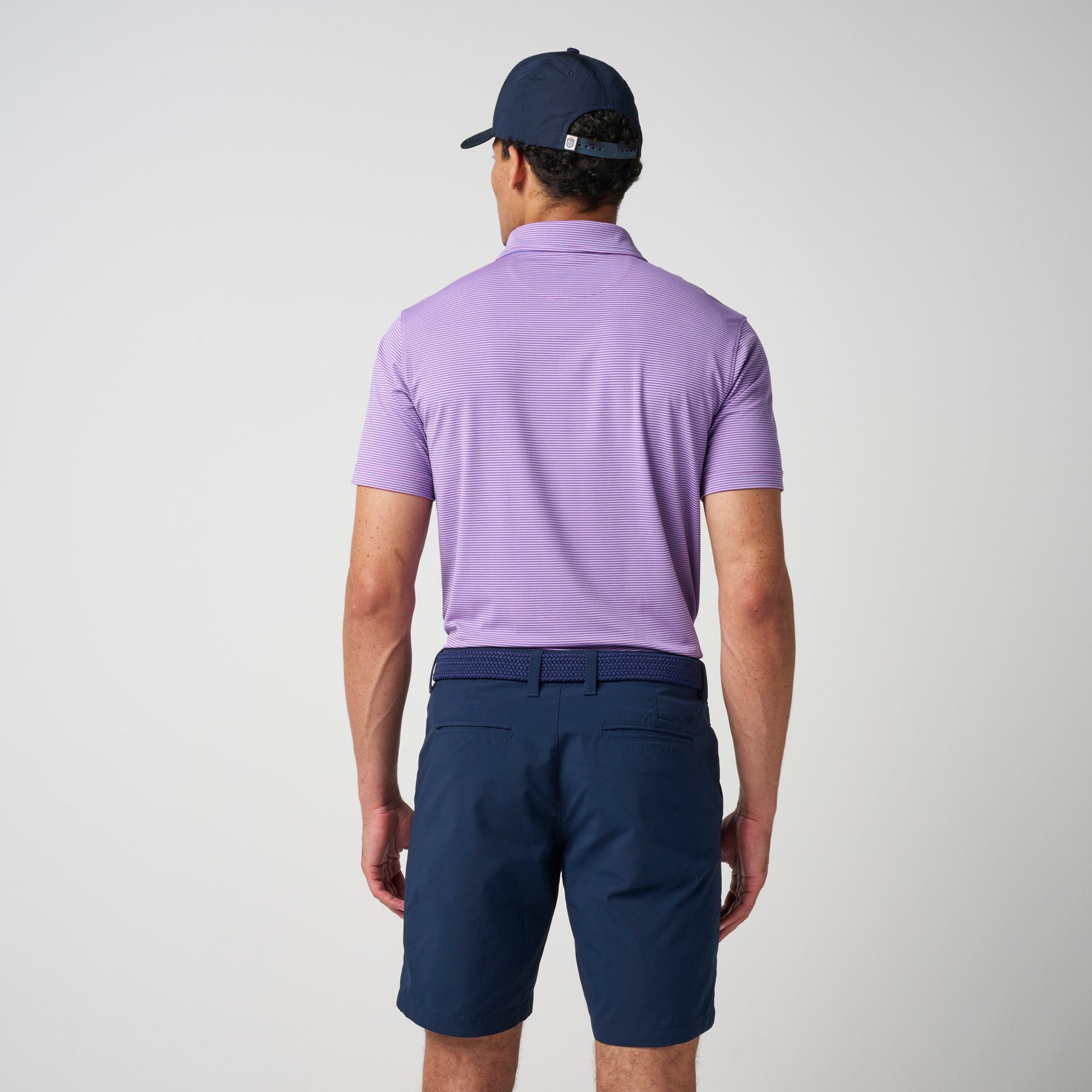 Man wearing lavender short-sleeve polo shirt with horizontal stripe texture and navy shorts, viewed from behind.