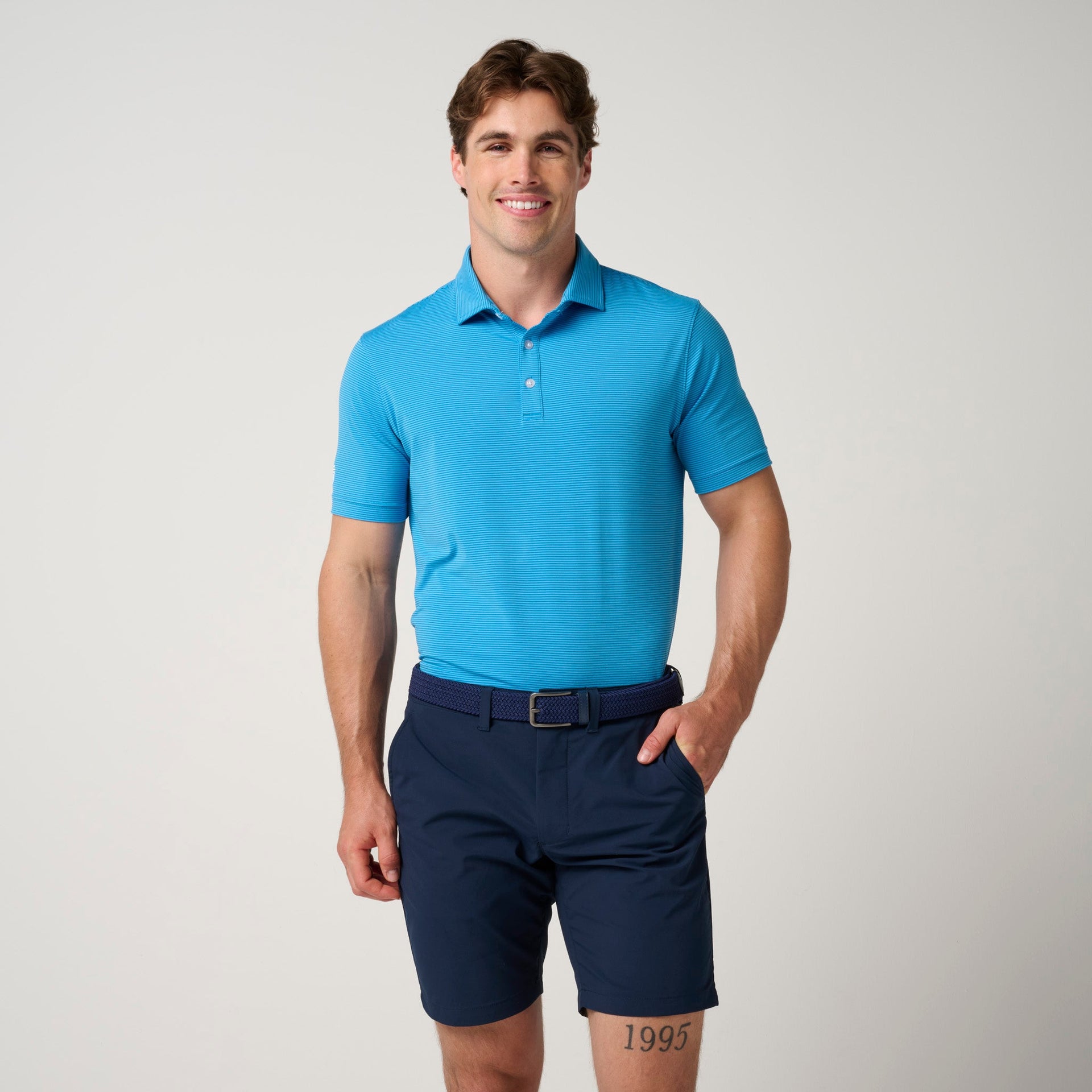 Man wearing bright blue striped polo shirt with collar and white buttons, paired with navy shorts and navy belt.